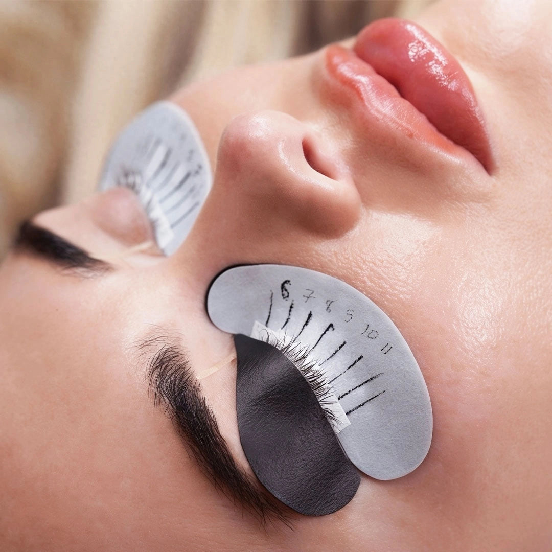 Close-up of a person's face with her eyes closed and eye patches underneath her eyes and on her eyelid.
