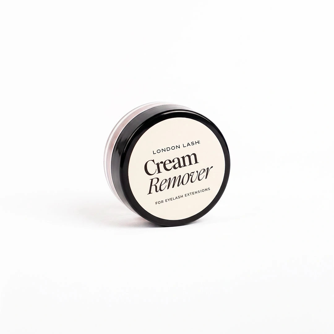 A small clear cosmetic jar containing pink cream remover, shown open with its black lid placed behind it on a clean white background. The lid label reads 'London Lash Cream Remover for Eyelash Extensions.
