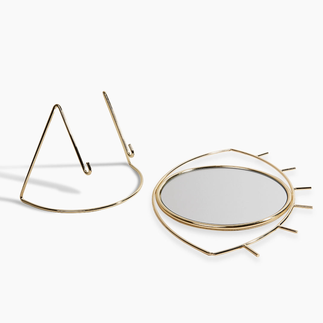 Eye shaped gold-framed mirror on a white background
