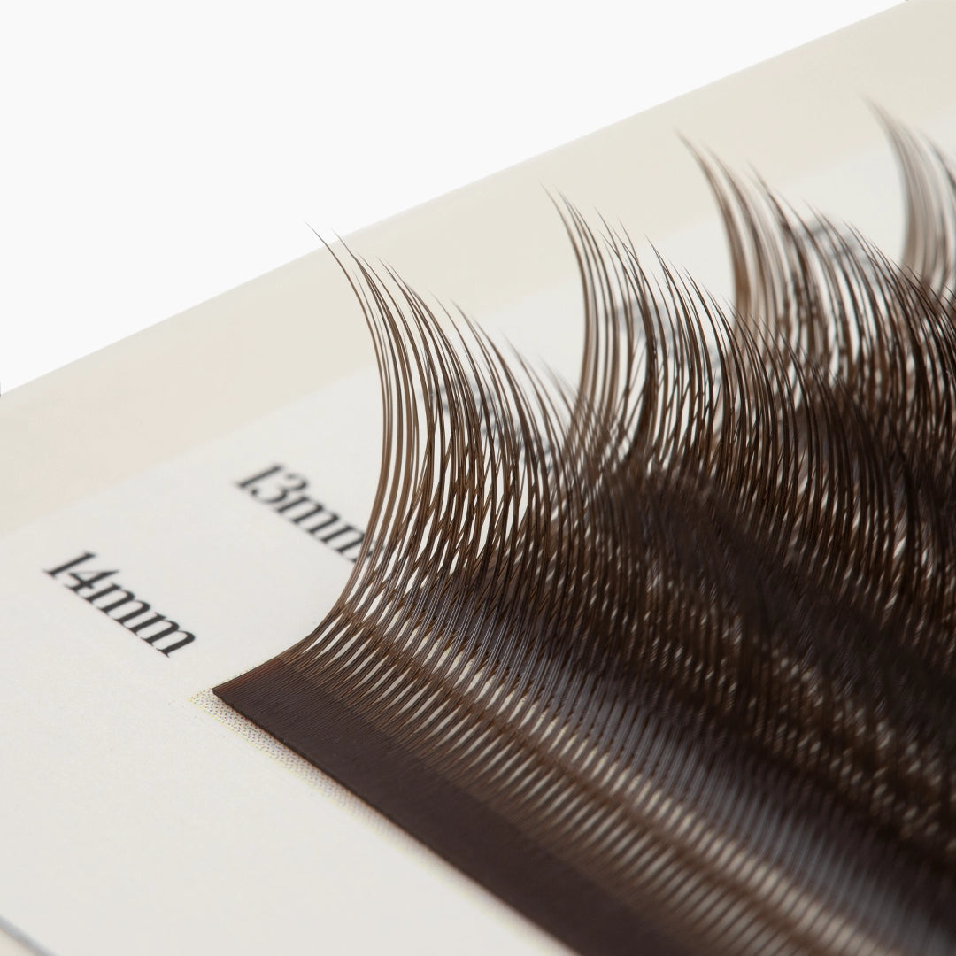 Macro close-up shot showing the upward curl and fine texture of brown Kitten Lash extension fibers on a 13mm to 14mm strip.