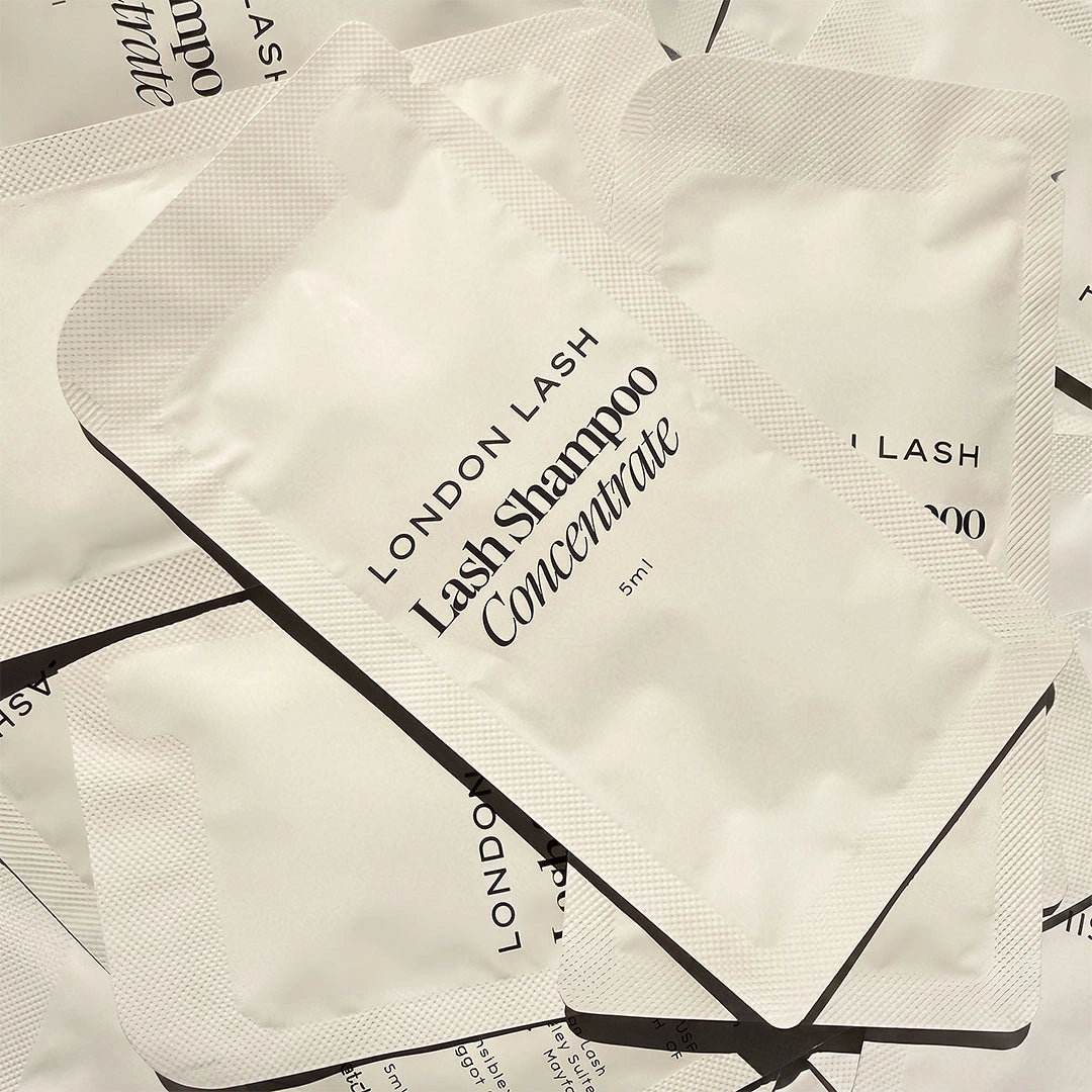 A pile of London Lash Lash Shampoo Concentrate 5ml single-use pouches, showing the white packaging with black text and borders.