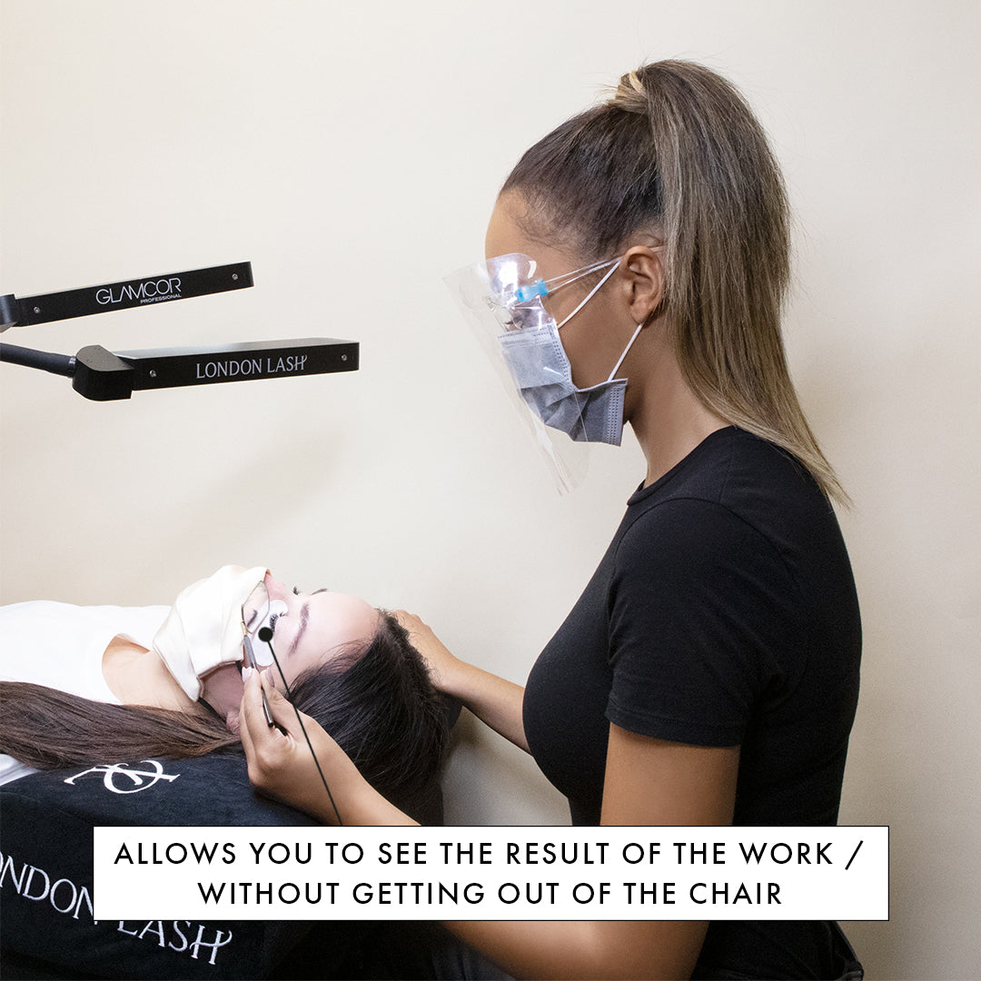 a lash technician sitting at a beauty bed using a lash mirror